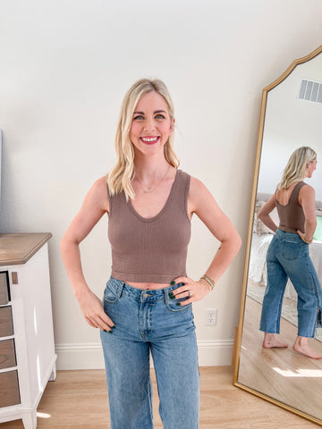 A woman modeling a mocha ribbed V-neck cropped tank paired with high-waisted blue denim. The tank features a minimalist design with a cropped fit and a flattering neckline, ideal for everyday wear.