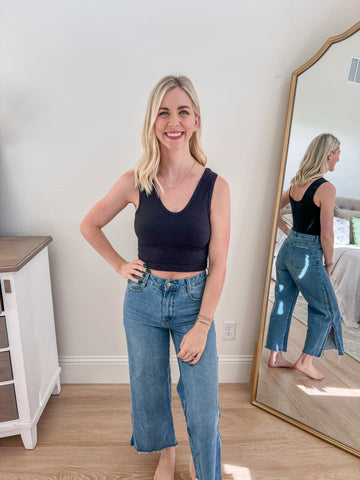 A woman modeling a black V-neck cropped tank paired with high-waisted blue jeans. The tank features a minimalist design with a flattering neckline and a soft, stretchy fit, perfect for layering or standalone wear.