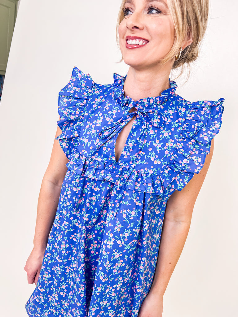 Woman wearing a blue floral babydoll dress with ruffle sleeves and a keyhole neckline.