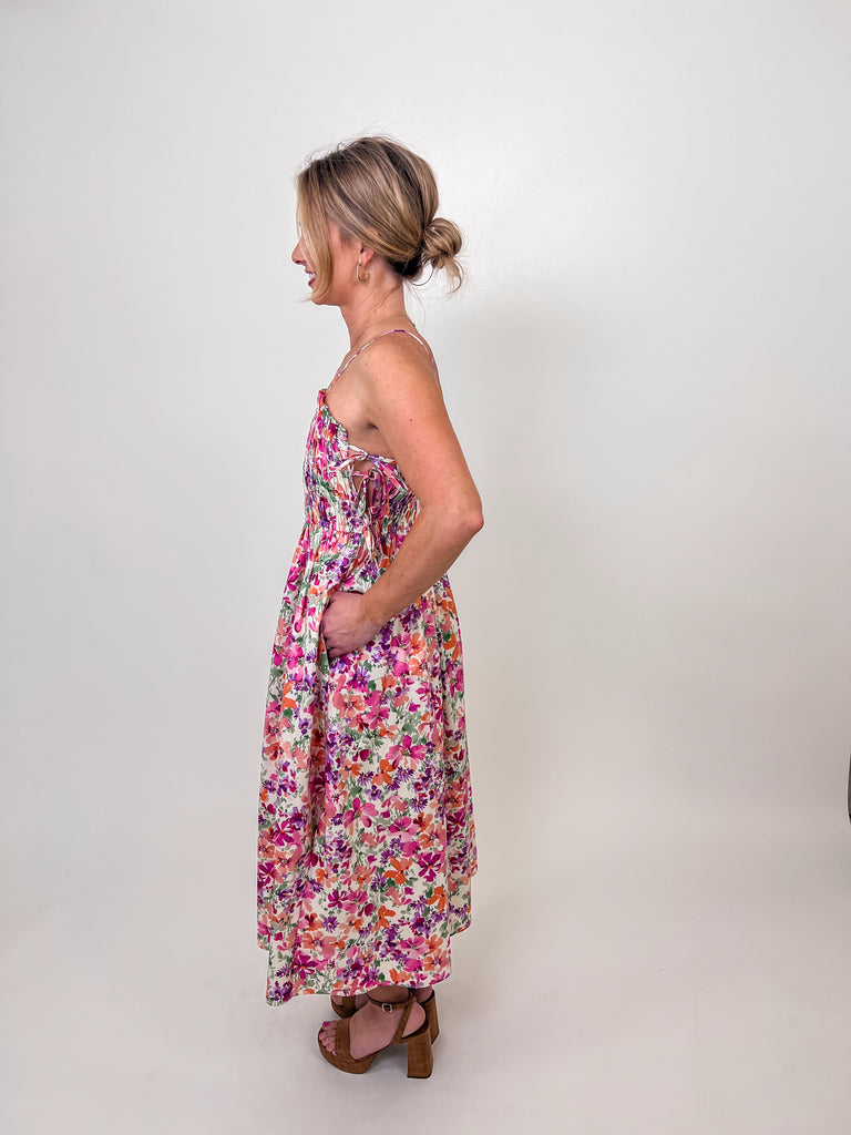 Woman wearing a floral smocked midi dress with tie straps and a flowy silhouette.