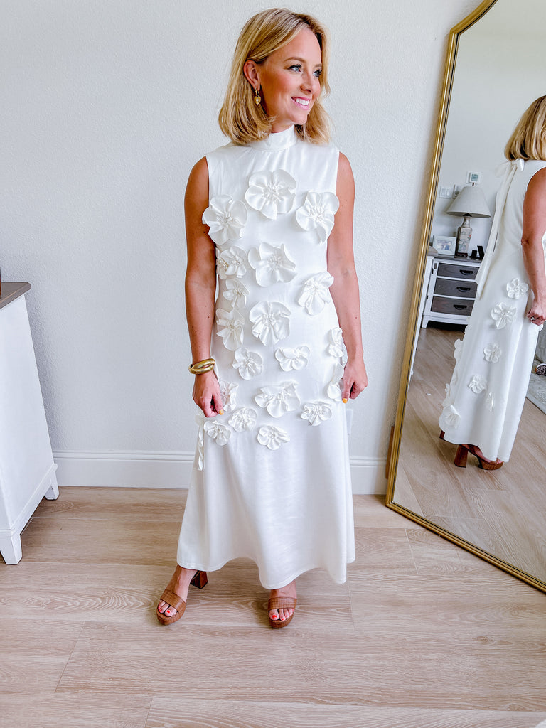White sleeveless maxi dress with 3D floral applique, available for purchase.
