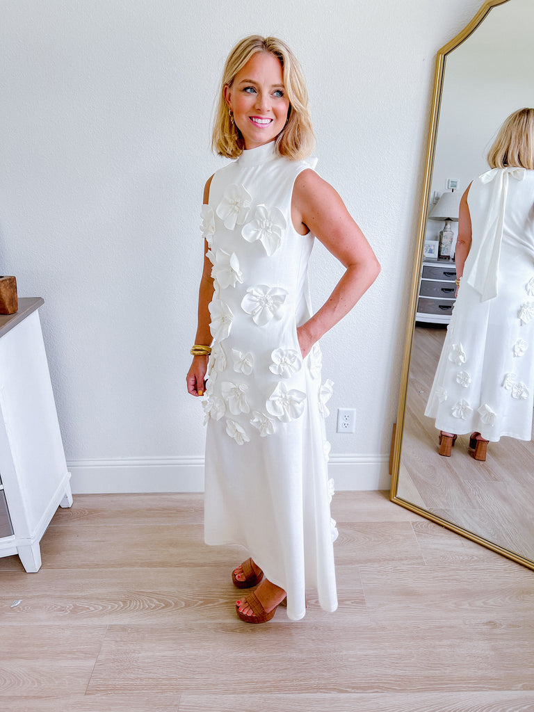 White sleeveless maxi dress with 3D floral applique, available for purchase.
