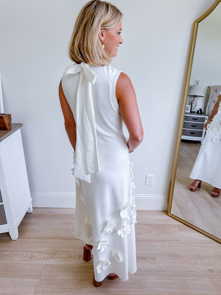 White sleeveless maxi dress with 3D floral applique, available for purchase.