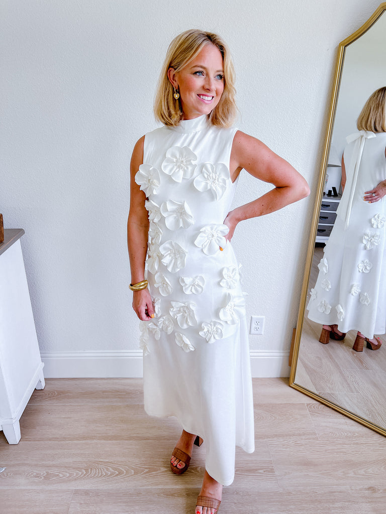 White sleeveless maxi dress with 3D floral applique, available for purchase.