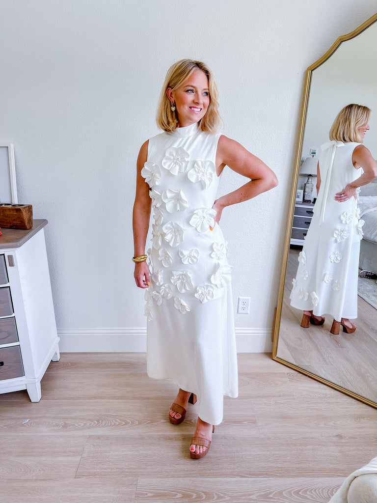White sleeveless maxi dress with 3D floral applique, available for purchase.