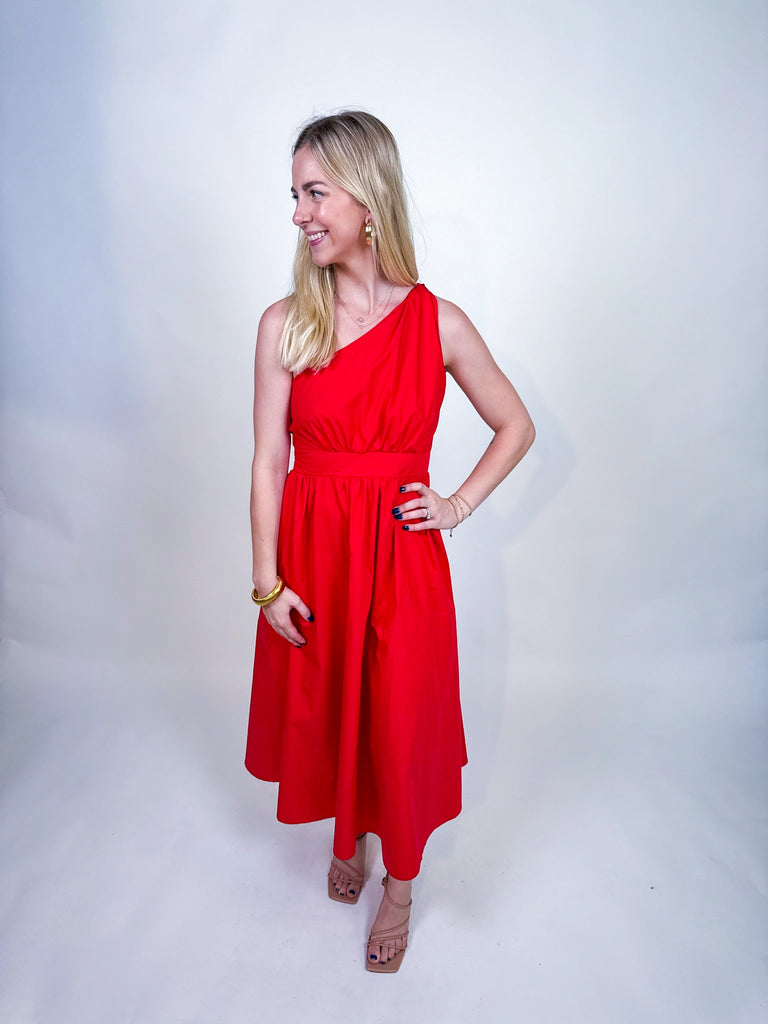 Woman wearing the Scarlet Spice Dress, a red one-shoulder midi with knotted strap and waist cutout.
