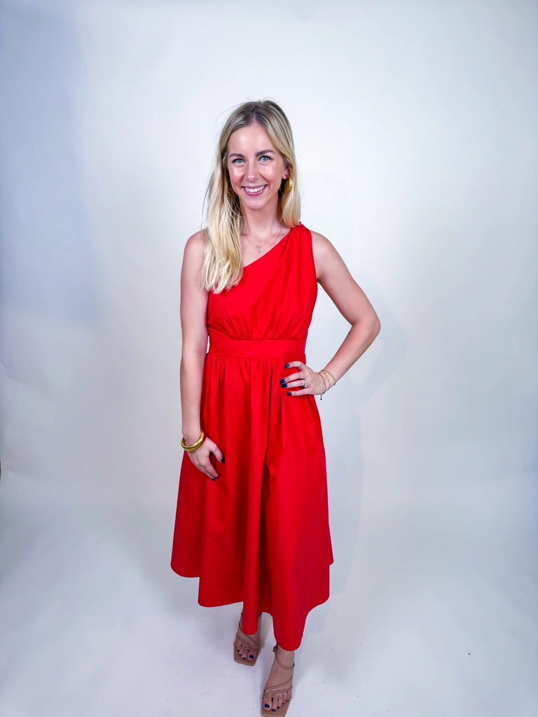 Woman wearing the Scarlet Spice Dress, a red one-shoulder midi with knotted strap and waist cutout.