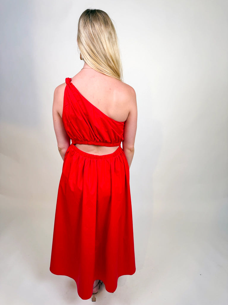 Woman wearing the Scarlet Spice Dress, a red one-shoulder midi with knotted strap and waist cutout.