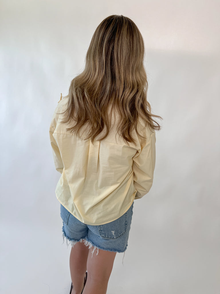Model wearing a pale yellow blouse with small bow details on the front and shoulder seams