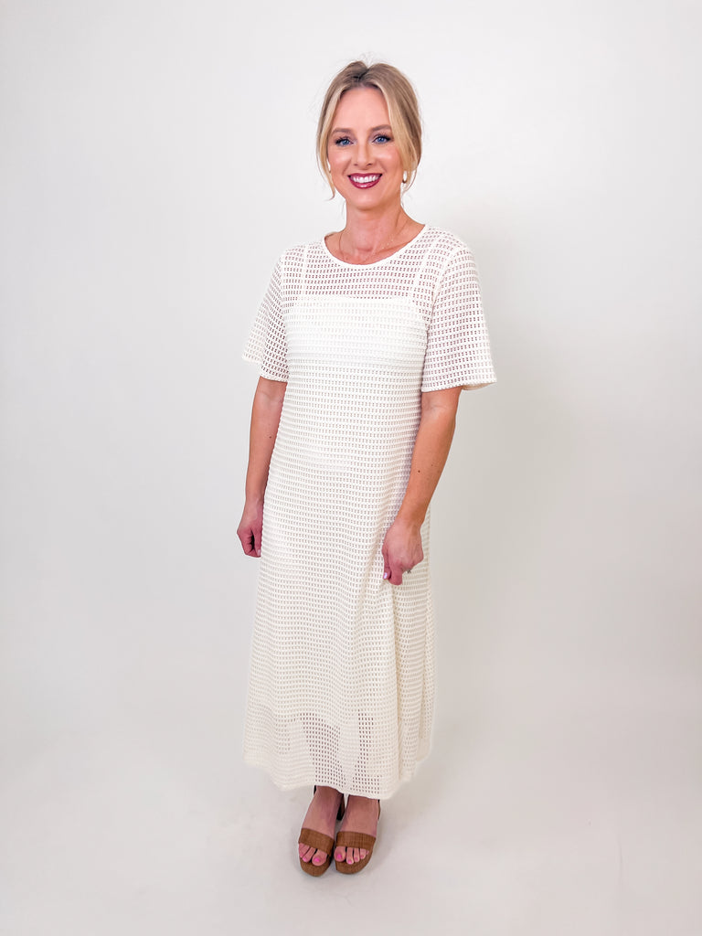 Woman wearing an ivory mesh maxi dress with short sleeves and a round neckline.