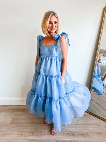 A light blue tiered maxi dress with ribbon tie straps, featuring a flowy, feminine design perfect for special occasions or everyday elegance. Styled with sparkling sandals, ideal for boutique shoppers seeking chic and airy fashion.