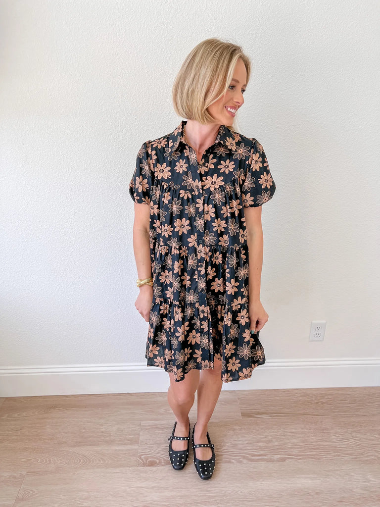 Women’s black babydoll dress with brown floral print, featuring short sleeves and a tiered design, available for purchase at an online boutique