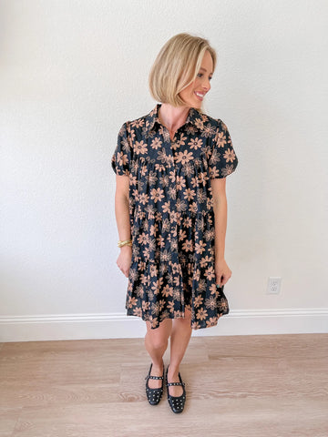 Women’s black babydoll dress with brown floral print, featuring short sleeves and a tiered design, available for purchase at an online boutique