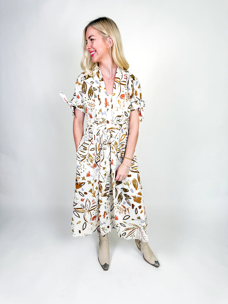 White midi dress with autumn-inspired abstract floral print, short sleeves with tie details, belted waist, and a flowy silhouette