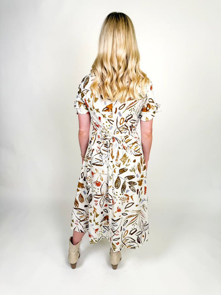 White midi dress with autumn-inspired abstract floral print, short sleeves with tie details, belted waist, and a flowy silhouette