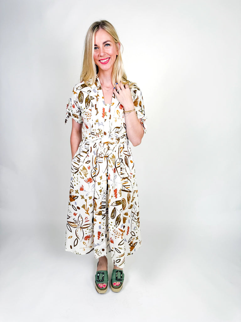 White midi dress with autumn-inspired abstract floral print, short sleeves with tie details, belted waist, and a flowy silhouette