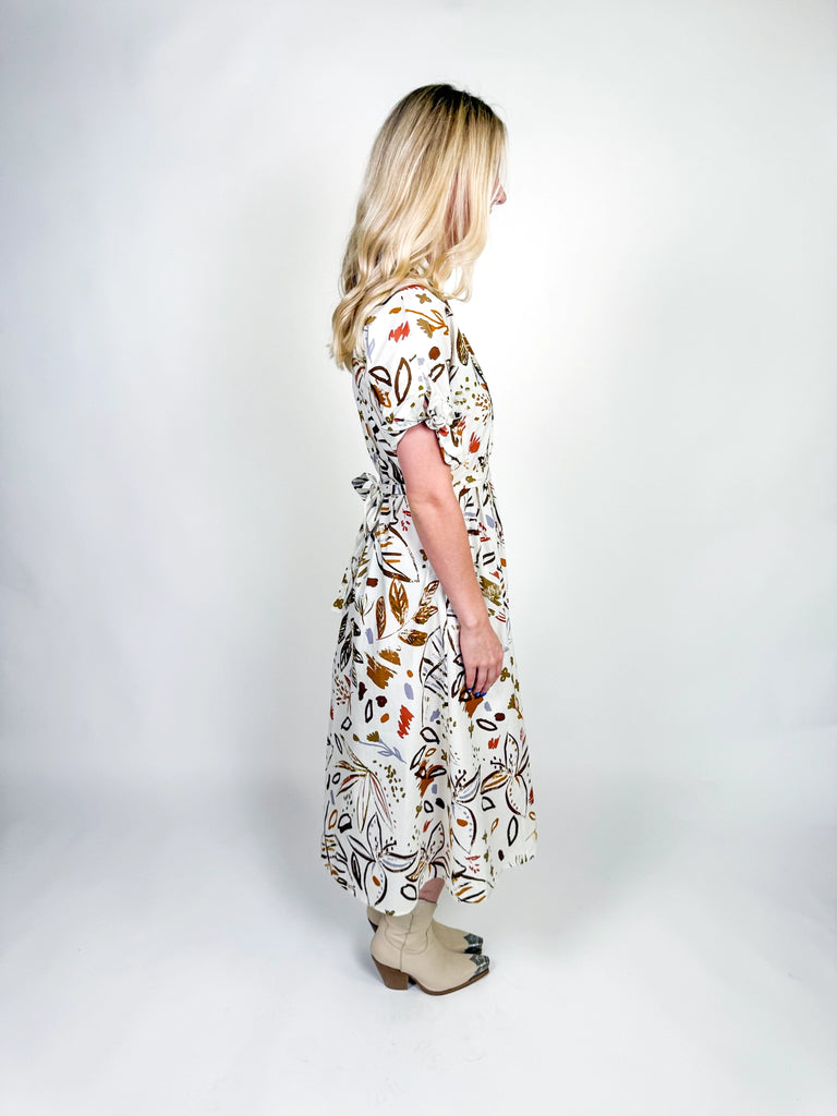 White midi dress with autumn-inspired abstract floral print, short sleeves with tie details, belted waist, and a flowy silhouette