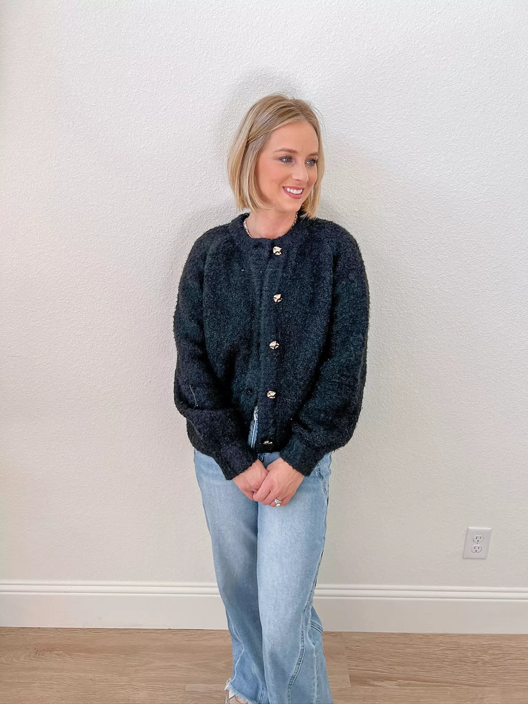 Soft black teddy cardigan with gold accent buttons, perfect for layering and creating cozy-chic looks, available now at our women’s boutique.