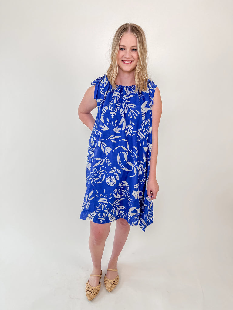 Woman wearing a blue shift dress with white lobster and crab print and tie-shoulder straps