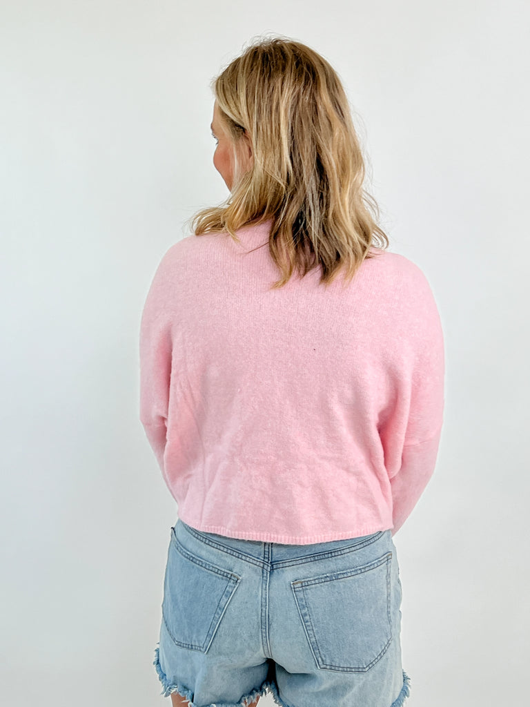 Pink button-up cardigan with pearl bow embellishments on front