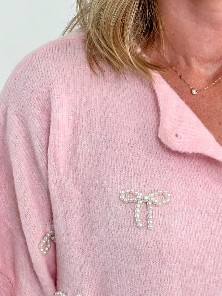 Pink button-up cardigan with pearl bow embellishments on front