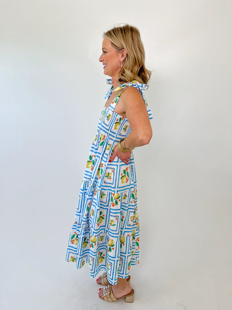 Woman wearing a lemon print smocked midi dress with tie straps and blue tile pattern