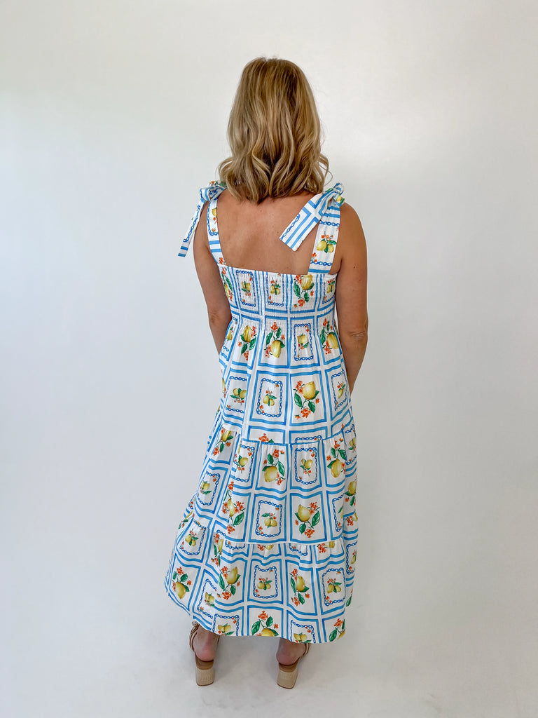 Woman wearing a lemon print smocked midi dress with tie straps and blue tile pattern