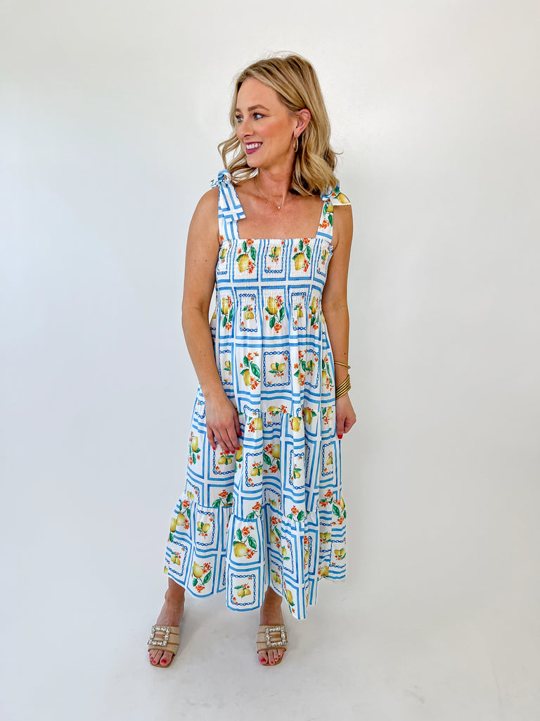 Woman wearing a lemon print smocked midi dress with tie straps and blue tile pattern