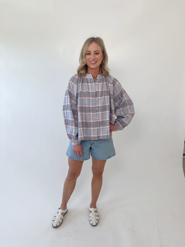 Woman wearing red, white, and blue plaid long sleeve blouse with gathered neckline and relaxed fit.