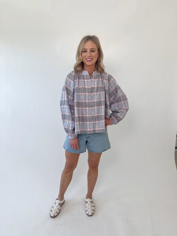 Woman wearing red, white, and blue plaid long sleeve blouse with gathered neckline and relaxed fit.