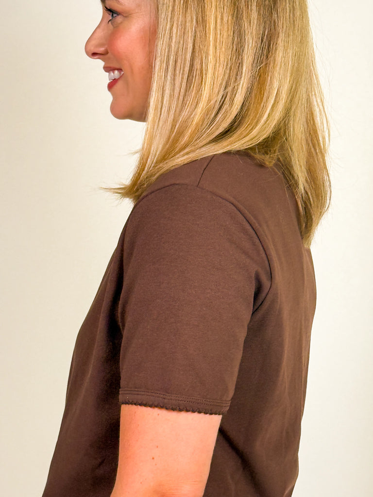 Woman wearing a cocoa brown short sleeve crew neck tee with scalloped hem detail