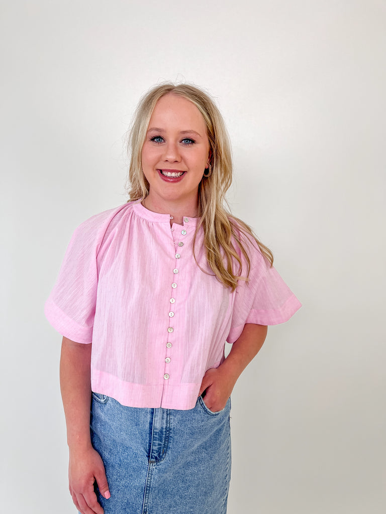 Woman wearing a cropped light pink blouse with short sleeves and pearl buttons