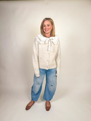 Woman wearing a cream knit cardigan jacket with oversized scalloped eyelet collar and bow tie closure