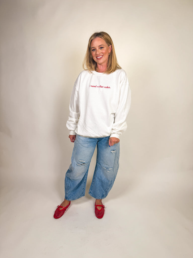 Woman wearing a white oversized sweatshirt with “i need a diet coke.