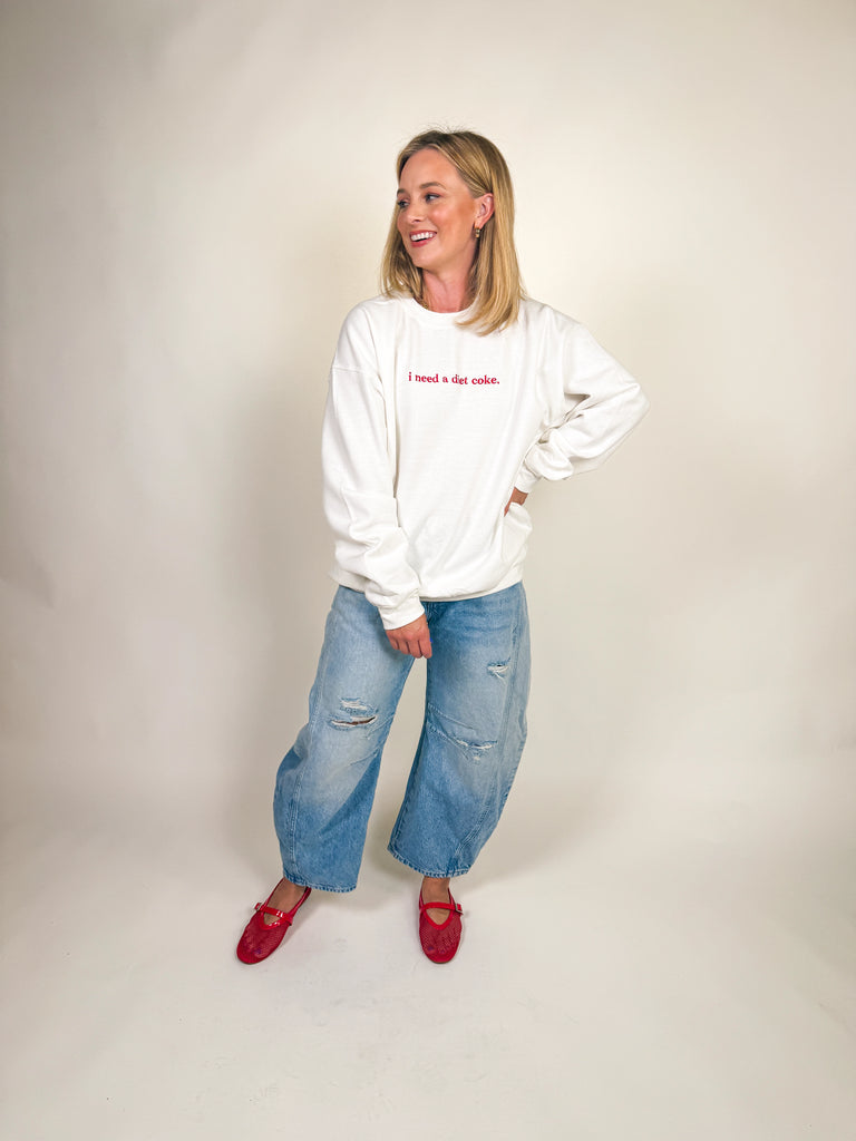 Woman wearing a white oversized sweatshirt with “i need a diet coke.