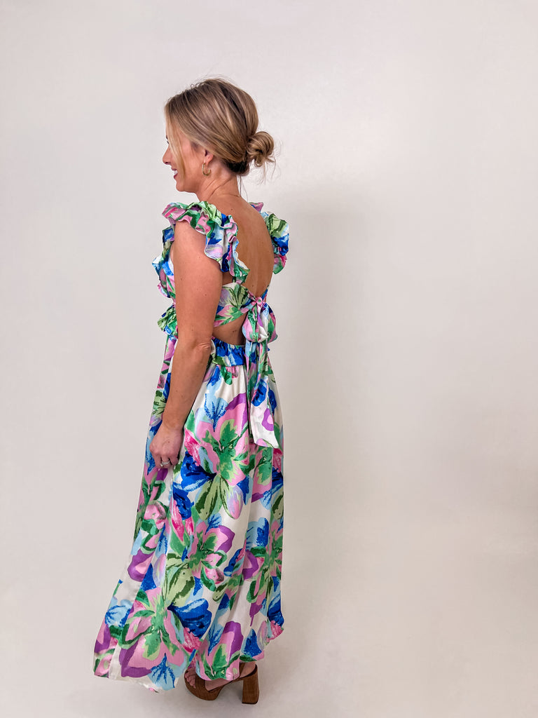 Woman wearing a floral ruffle maxi dress with an open back and self-tie bow.