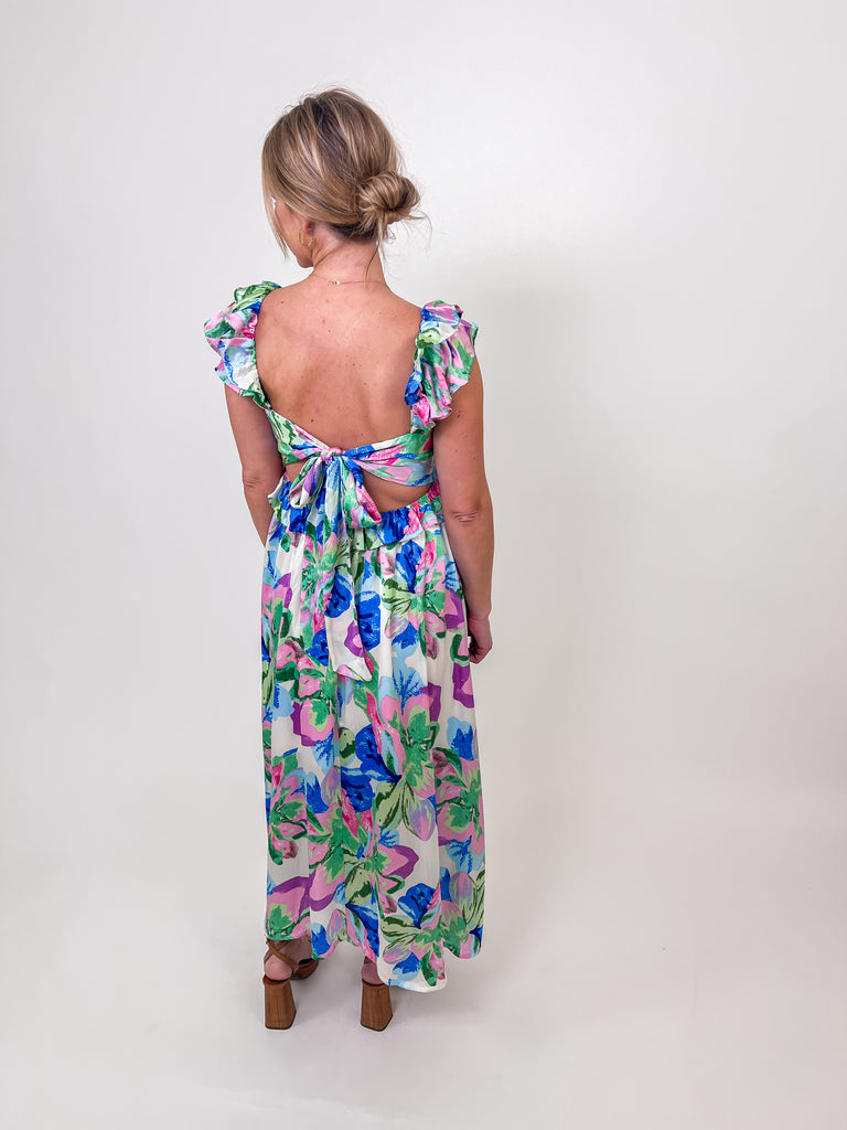 Woman wearing a floral ruffle maxi dress with an open back and self-tie bow.