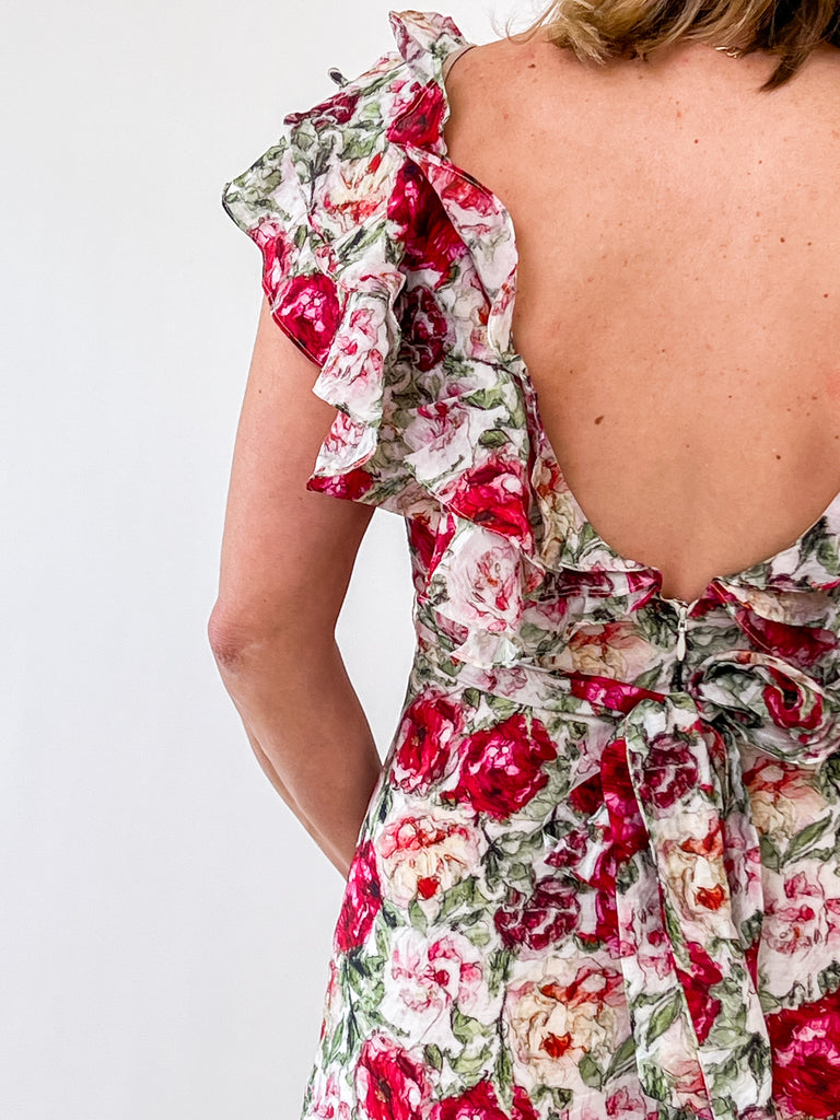 Woman wearing a floral ruffle midi dress with an open back and self-tie bow.