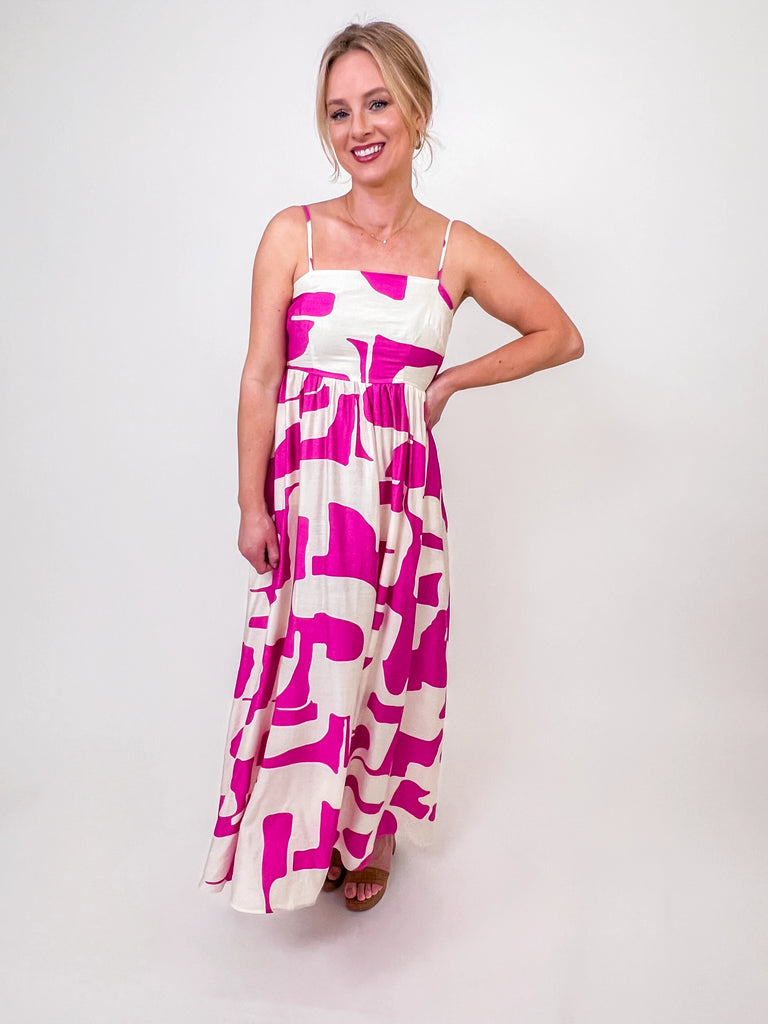 Woman wearing a fuchsia and ivory abstract print maxi dress with spaghetti straps and a smocked back.