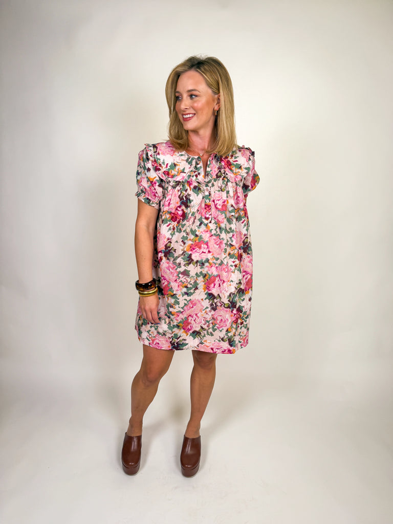 Woman wearing a floral pink mini dress with ruffle neckline and short sleeves