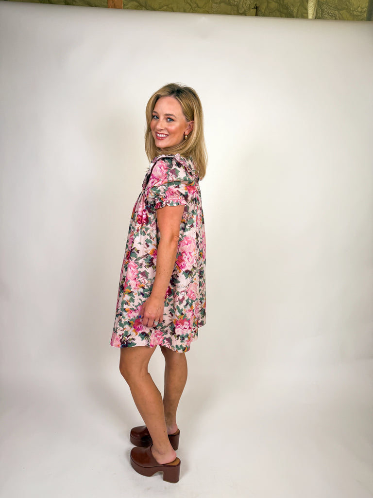 Woman wearing a floral pink mini dress with ruffle neckline and short sleeves