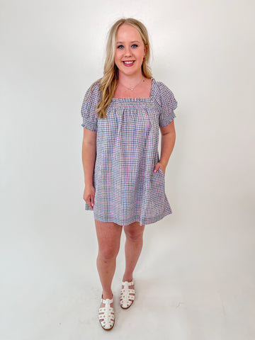 Woman wearing a puff sleeve babydoll mini dress with pink and blue gingham print and square neckline
