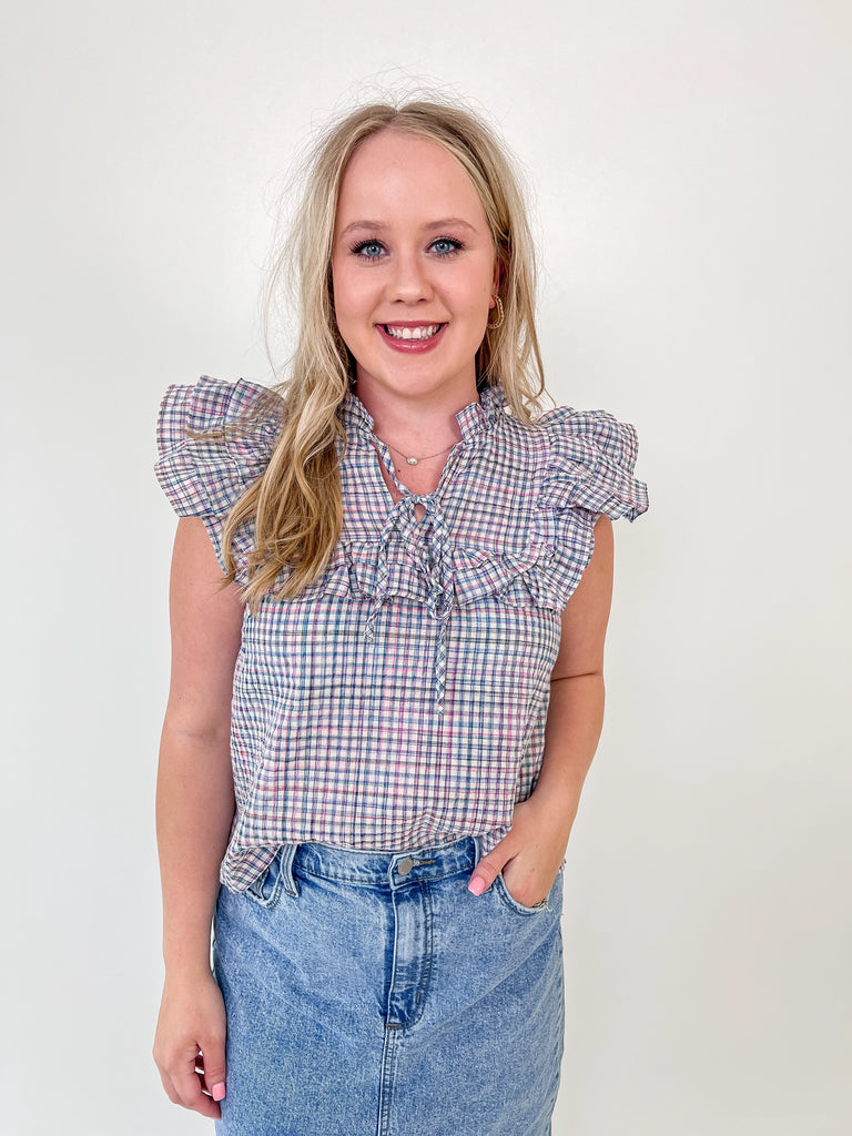 Woman wearing a sleeveless plaid blouse with ruffle shoulders and front tie detail