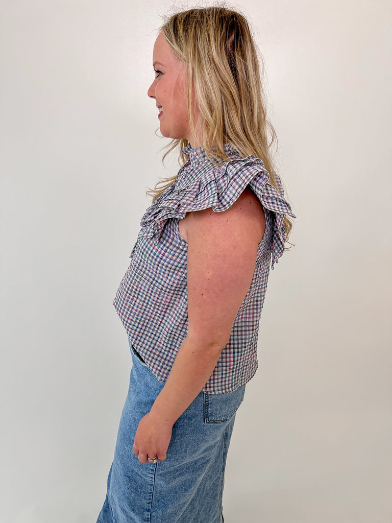 Woman wearing a sleeveless plaid blouse with ruffle shoulders and front tie detail