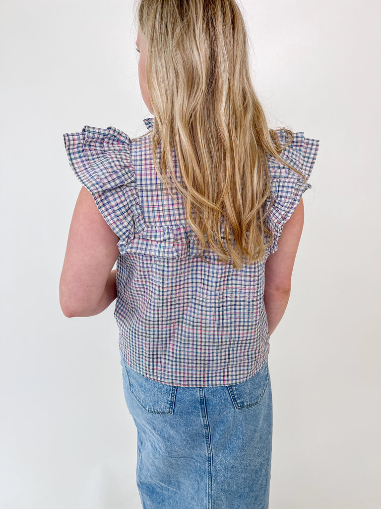 Woman wearing a sleeveless plaid blouse with ruffle shoulders and front tie detail