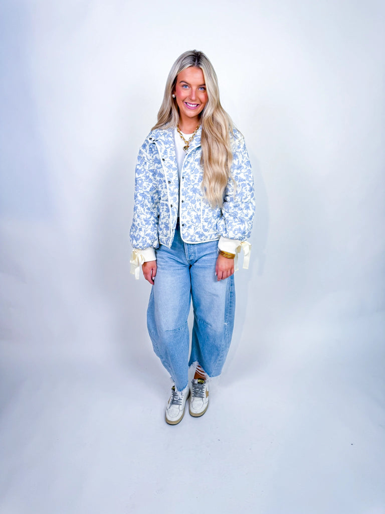 Woman wearing the Glacier Petal Jacket, a blue-and-white floral quilted jacket with ribbon-tie cuffs.