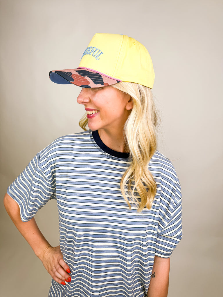 model wearing Grateful Baseball Cap with yellow front, blue embroidered text, cheetah print bill, and pink snapback