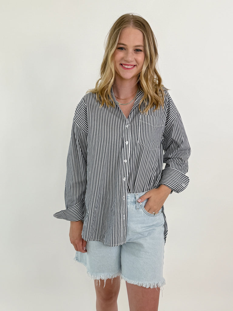 Woman wearing a grey and white vertical striped oversized button-down shirt