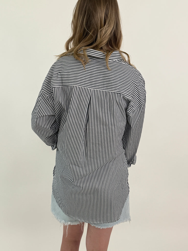 Woman wearing a grey and white vertical striped oversized button-down shirt