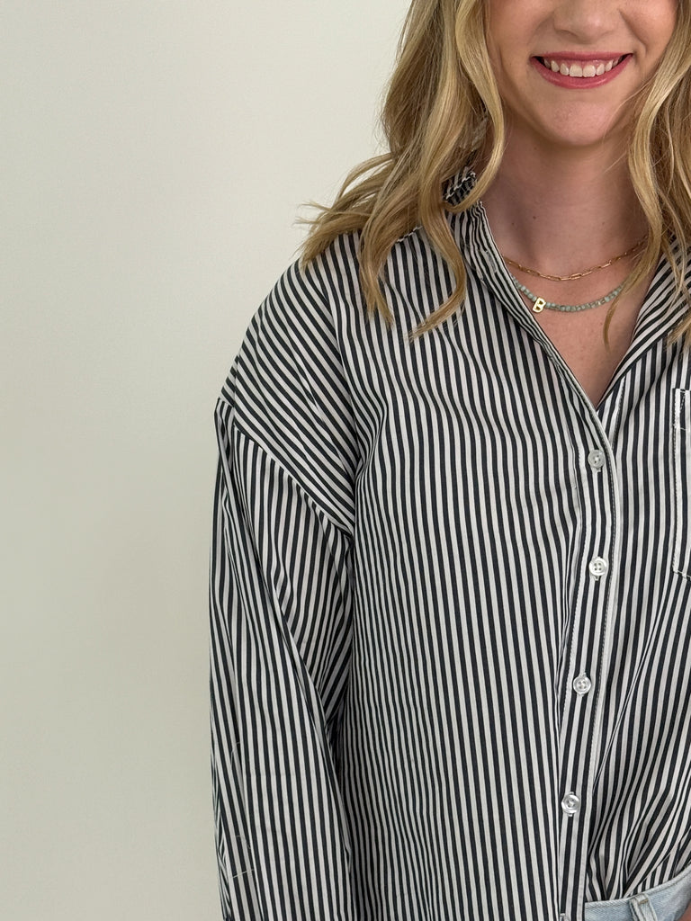 Woman wearing a grey and white vertical striped oversized button-down shirt